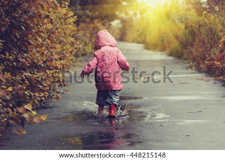 Toddler girl in pink jacket jumping in puddles after summer rain. color corrected vintage style picture