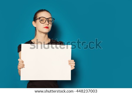 Pretty young woman showing on empty blank board. Colorful studio portrait isolated on blue background. Space for text