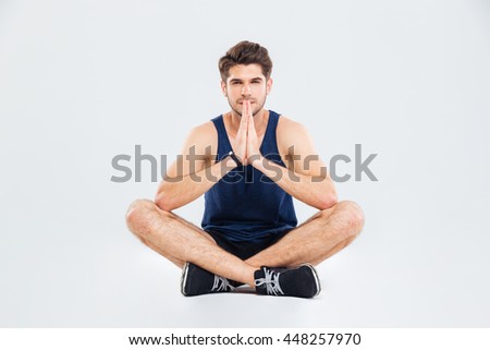 Handsome young sports man sitting and doing yoga over white background