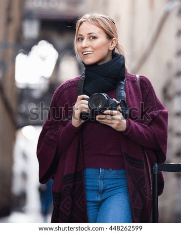 Charming smiling woman looking curious and taking pictures outdoors