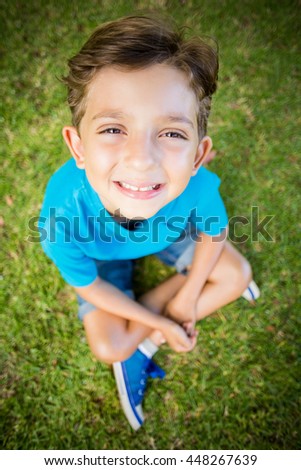 Portrait of young boy sitting on grass and smiling at camera in park