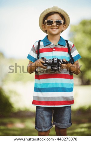 Smiling young boy in sunglasses holding a camera in park