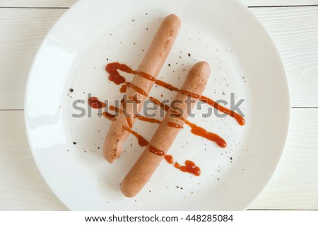Two sausages white plate ketchup top view on white wooden background