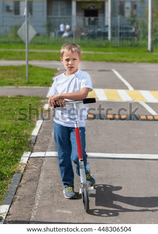 The boy on the scooter, standing on the street in the summer, on the roadway, traffic, pedestrian crossing, photography where the boy as a member of the movement