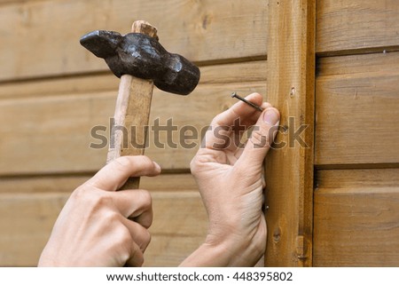 hands hammering nail in plank, closeup