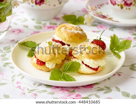 Cream puffs cakes or profiterole filled with whipped cream, powdered sugar topping and served with strawberries on the table
