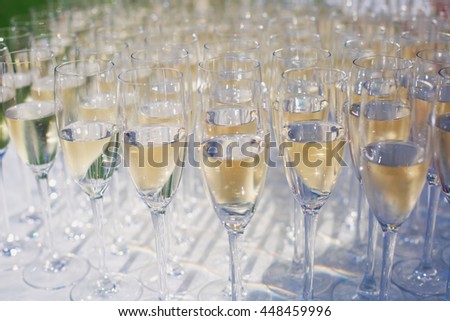 Beautiful row line of gold yellow colored glasses with champagne on a party, on decorated catering bouquet table on open air event, picture with beautiful bokeh
