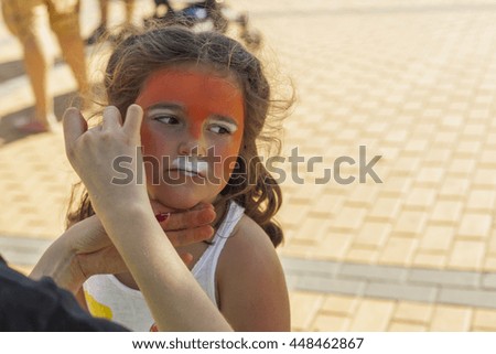 Girl getting her face painted by painting artist. Outdoor children party. 