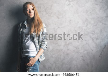 Casually dressed, pretty young woman standing against blank concrete wall. Mock up
