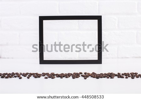 Front view of bright table with coffee beans and blank see-through picture frame on white brick wall background. Mock up