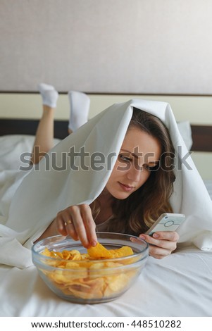 Girl eating chips in bed and watching news in phone
