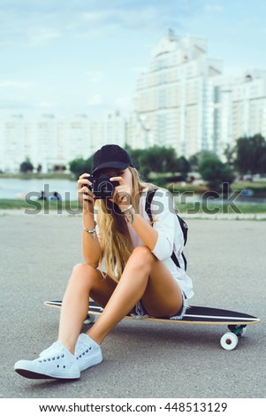 Beautiful young woman seating on skate and make self photo, street fashion lifestyle. outdoor portrait, posing in the street on hat, sneakers, 