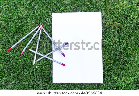 Multicolor pencils, paper sheet on fresh green grass field. Flat lay