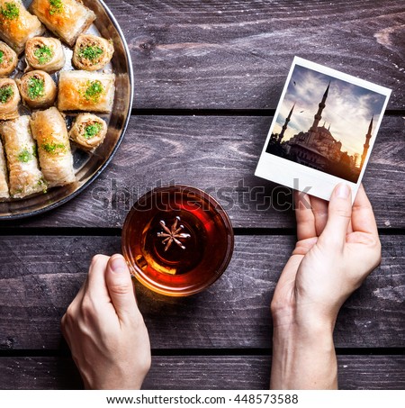 Hands with photo of Blue mosque in Istanbul and black tea near Turkish baklava on wooden background  