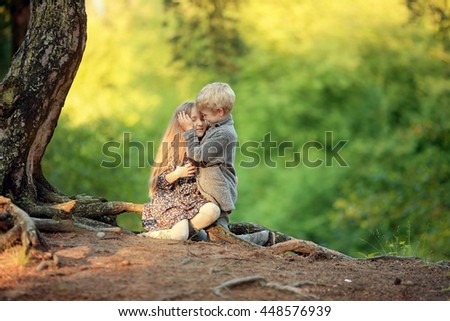 boy in a suit playing a girl with long curly hair and dress sitting on a tree root in the forest