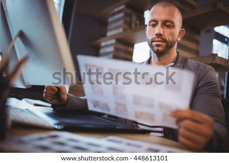 Businessman looking at photographs while using graphics tablet in creative office