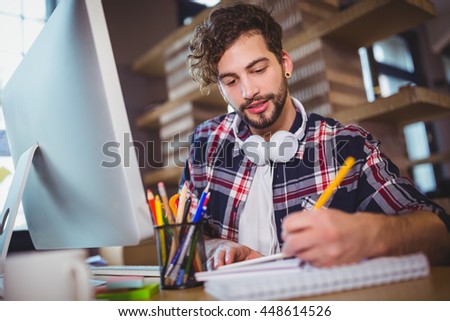 Creative businessman writing in spiral notebook on computer desk at office