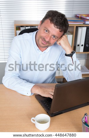 Cheerful businessman thinking and looking at camerasitting in a desk at office Royalty-Free Stock Photo #448647880