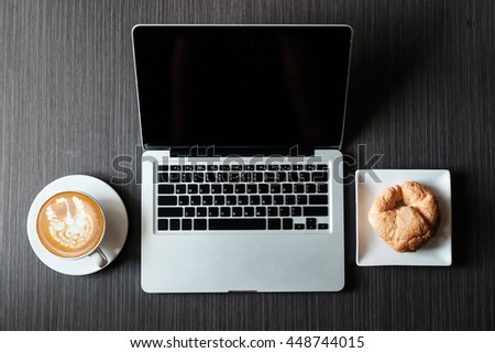 coffee, laptop and croissants to show a business breakfast on the back desk in morning