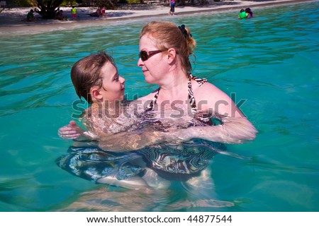 young happy boy with brown hair enjoys swimming and hugging with his mother  in the beautiful sea