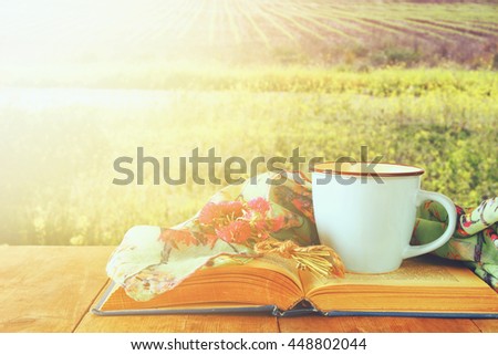 Fashion scarf with cup of coffee and old book on a wooden table in front of summer morning sunlight. Vintage filtered