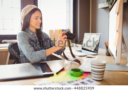Female graphic designer looking at pictures in digital camera at office