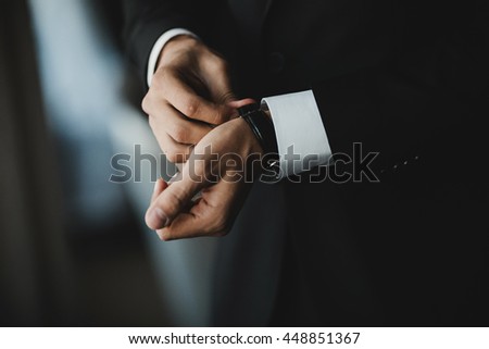 Gentleman in black suit puts on a black watch Royalty-Free Stock Photo #448851367