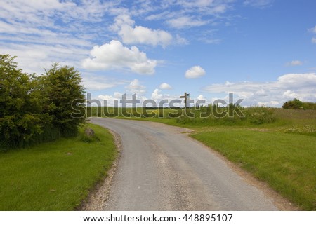 a farm road with a wooden footpath sign in the yorkshire wolds under a blue cloudy sky in summer