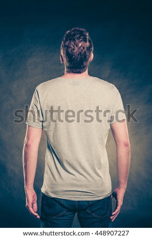Back rear view of fashionable man in blank shirt with empty copy space. Guy in studio on black. Casual fashion advertisement. Instagram cross filter.