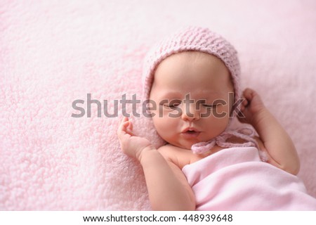 Portrait of a cooing, two week old, newborn baby girl. She is wearing a knitted bonnet and is lying on a soft, fuzzy, pink blanket. Royalty-Free Stock Photo #448939648