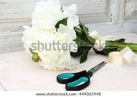 Fresh bright bouquet of white peony with scissors and satin ribbon on aged white wooden background. floral decor elements in a rustic setting