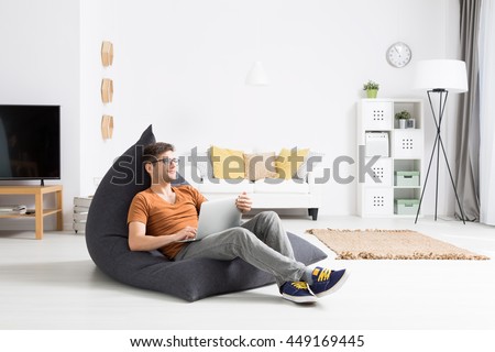 Young man relaxing comfortably in a grey sitting sack in a bright studio flat Royalty-Free Stock Photo #449169445