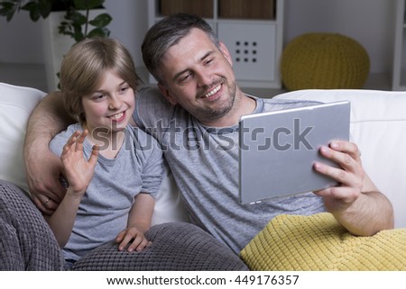 Happy father and his small son sitting on a sofa and watching something on tablet device