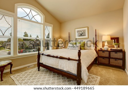 Cozy Beige bedroom with vaulted ceiling, large window and elegant Victorian style bed.