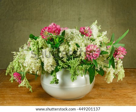 Alfalfa, meadowsweet. Still life. Bouquet of meadow flowers in white pots standing on a wooden table. Rustic style.
