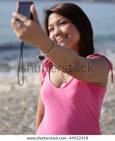 Pretty young asian woman taking a self-portrait while outdoors on a beach on a summer day