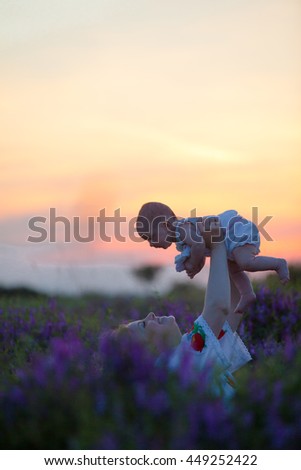 Beautiful young mother tenderly holding up her little adorable baby at sunset in a field