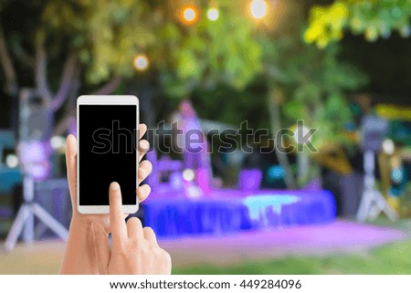 woman use mobile phone and blurred image of a man sing on the stage in night party