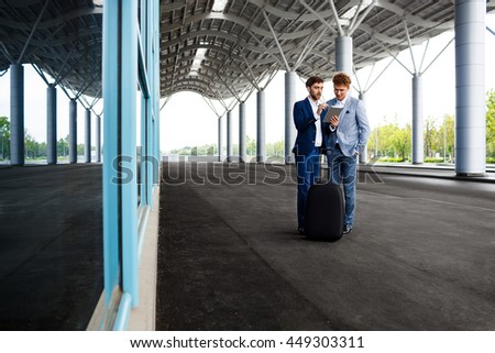 Picture of  two young businessmen talking on airport background and holding tablet