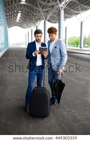 Picture of  two young businessmen talking on airport background and holding tablet 