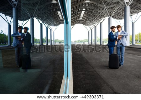 Picture of  two young businessmen talking on station  background and holding tablet reflected in window