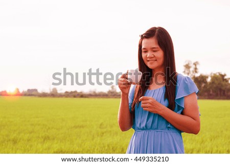 Woman wearing a blue dress holding a cup coffee . At the sunset.