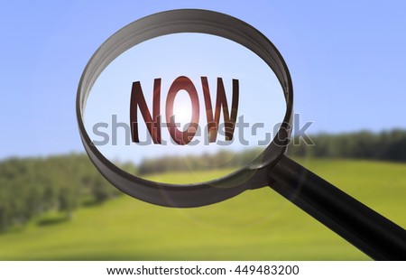 Magnifying glass with the word now on blurred nature background