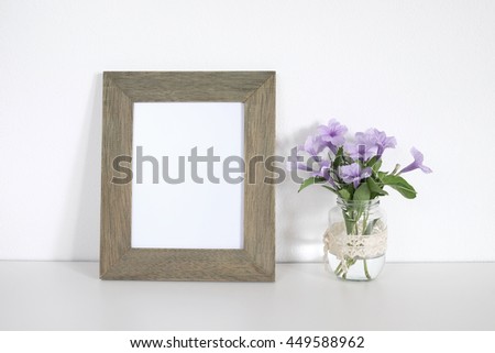 Blank wooden frame with flower in vase on table and white wall background