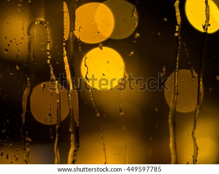Raindrops and water trickling down a window pane with de-focused street lights in the back