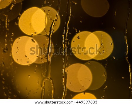 Raindrops and water trickling down a window pane with de-focused street lights in the back