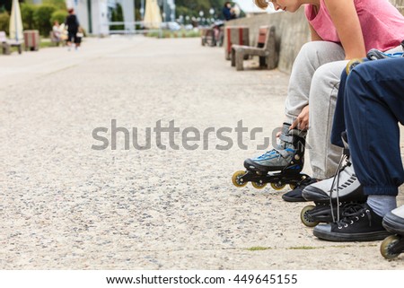 Closeup of people friends putting on roller skates outdoor. Woman and man sitting on bench.