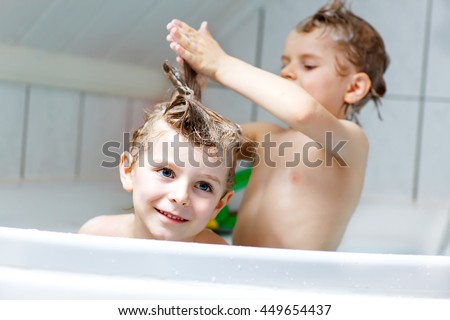 Happy siblings: Two little twins children playing together with water by taking bath in bathtub at home. Kid boys having fun together.