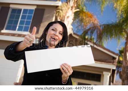 Happy Attractive Hispanic Woman with Thumbs Up Holding Blank Sign in Front of House.