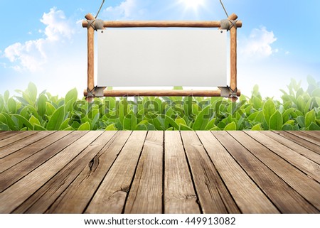 Wood table with hanging wooden sign on green leaves background
